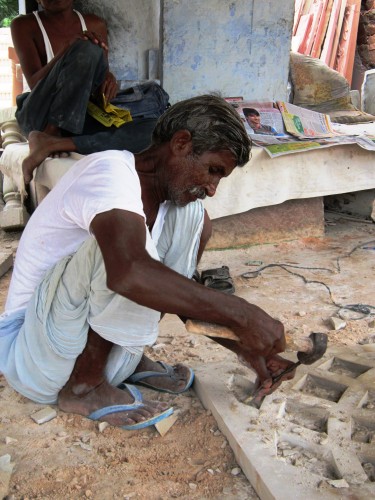 A stonecutter squats, hammer and chisel in hand, in one of the many shops along the road from Agra to Jaipur.