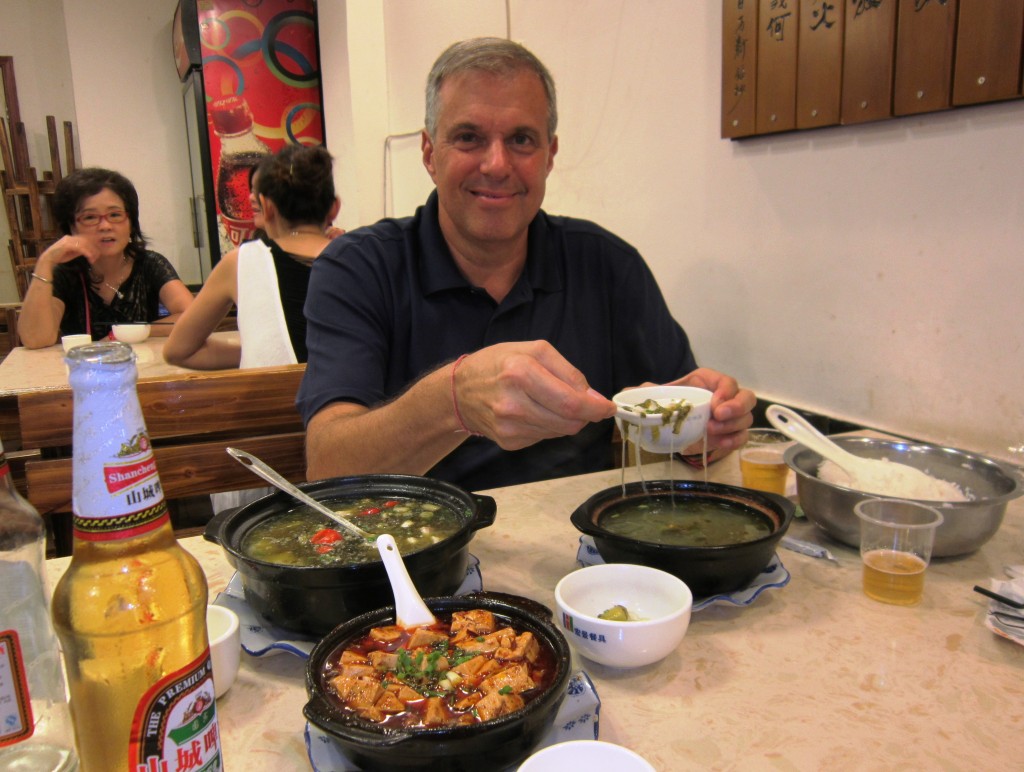 Happy guy surrounded by spicy food. That's the duck blood tofu in foreground.